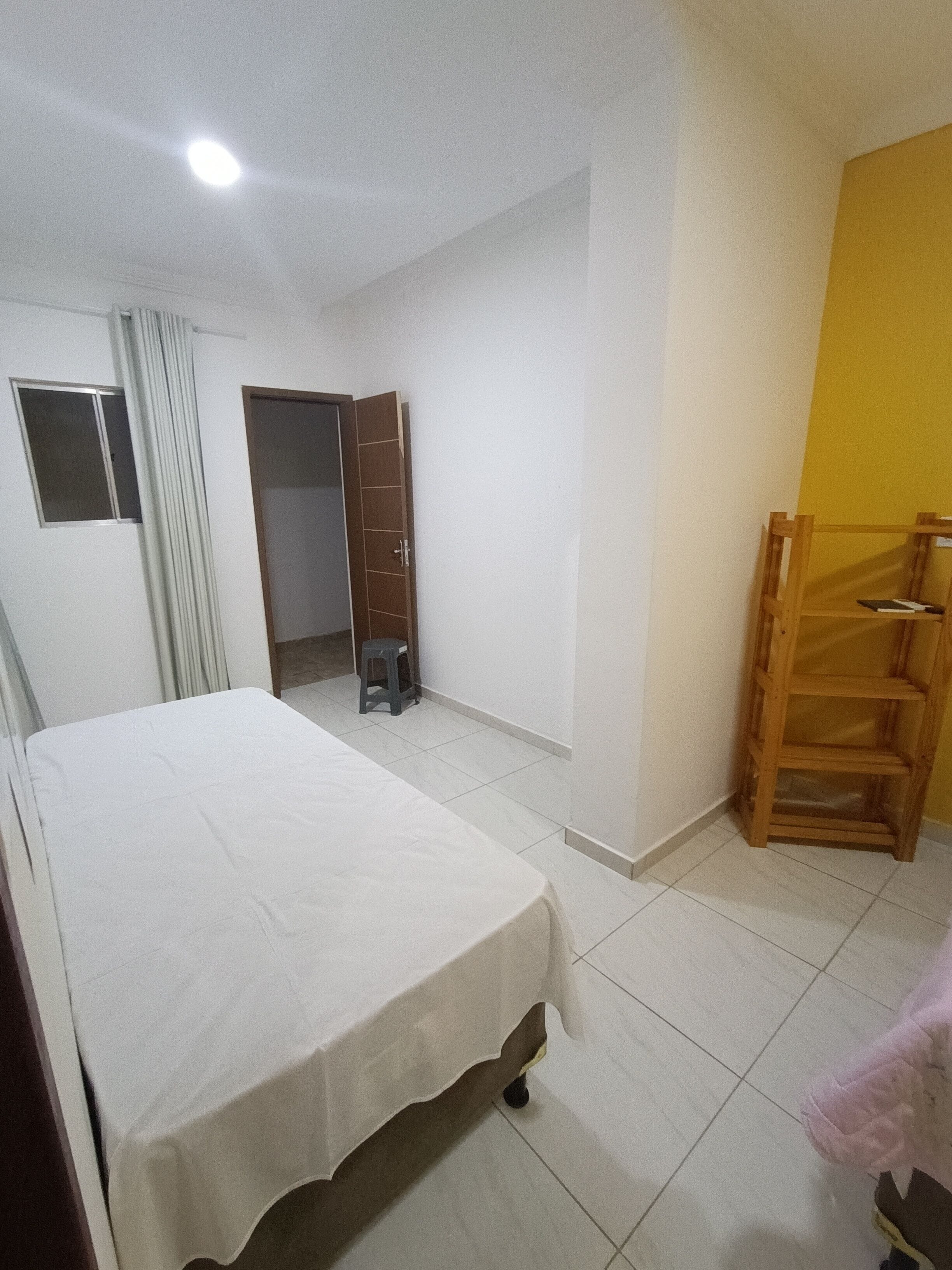 A bedroom with a bed, a wooden chair, a wardrobe, and a small stool.