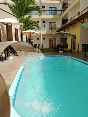 A swimming pool with a water slide, surrounded by outdoor seating and palm trees. - Pousada Canto dos Corais Maragogi (Maragogi)