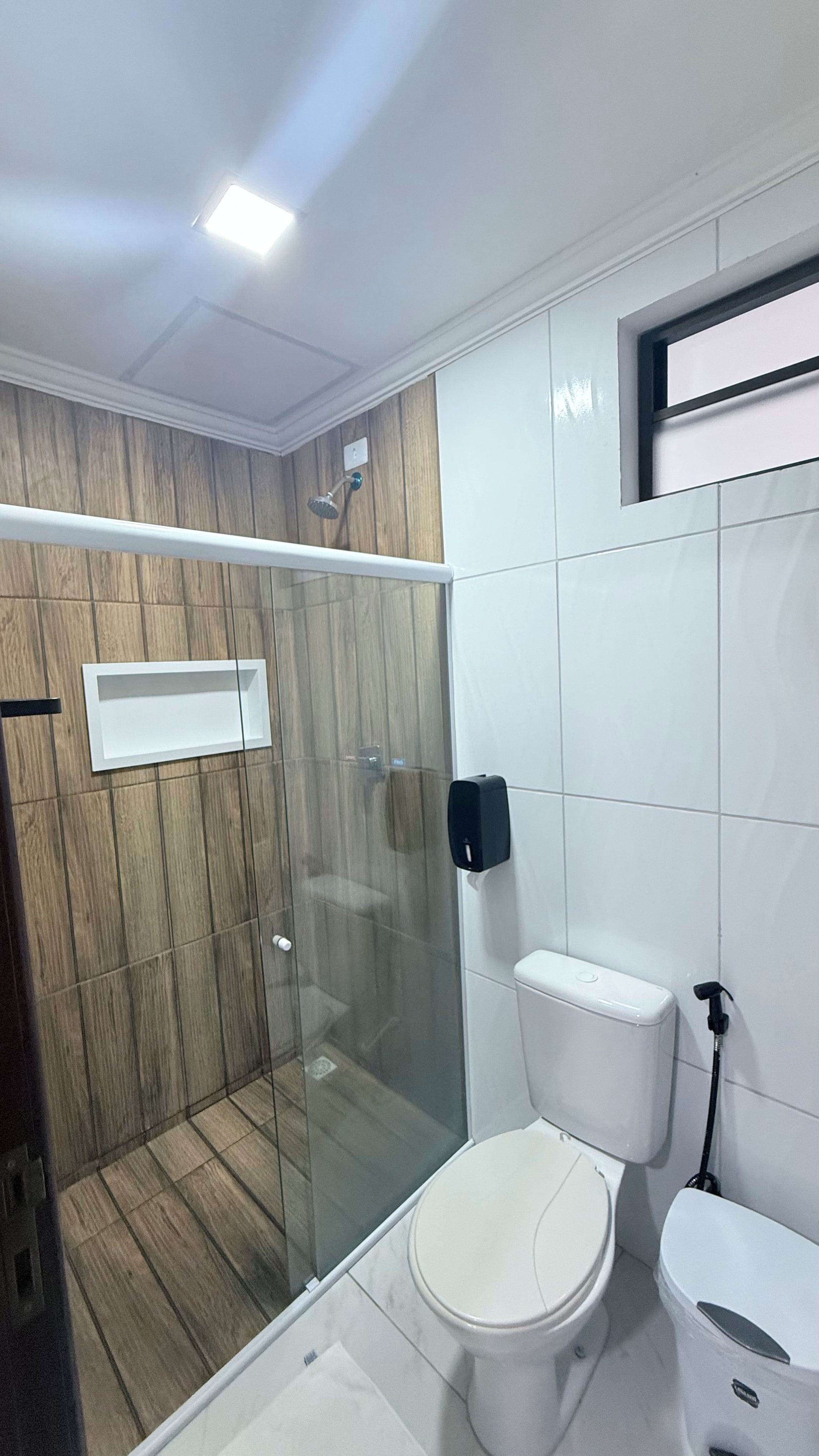 Un baño con ducha de vidrio, inodoro y dispensador de jabón.