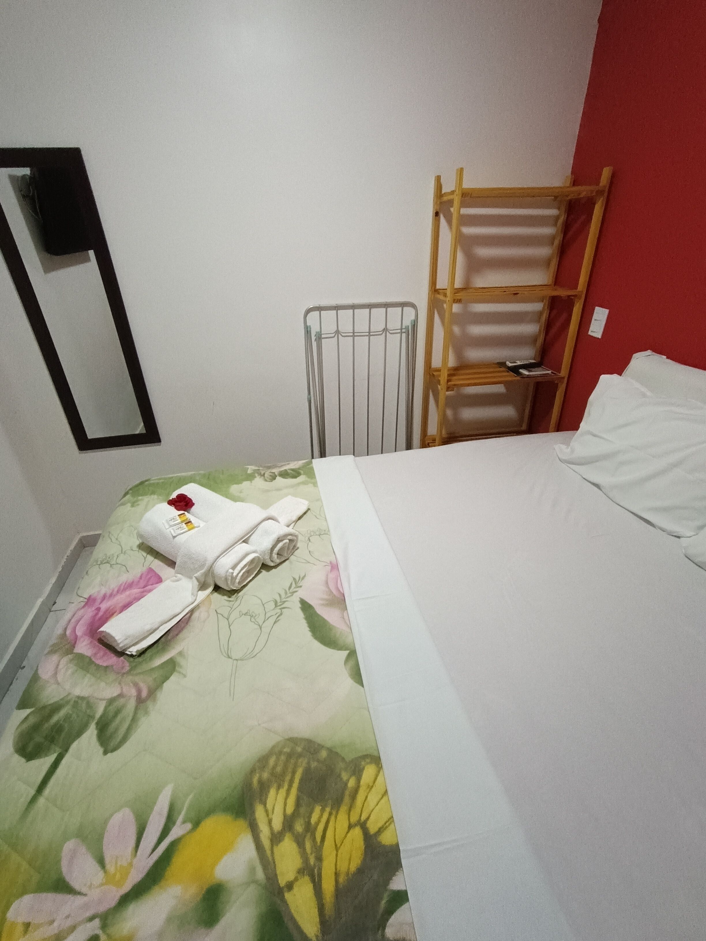 A hotel room with a bed, a wooden ladder, a metal rack, and a mirror on the wall.
