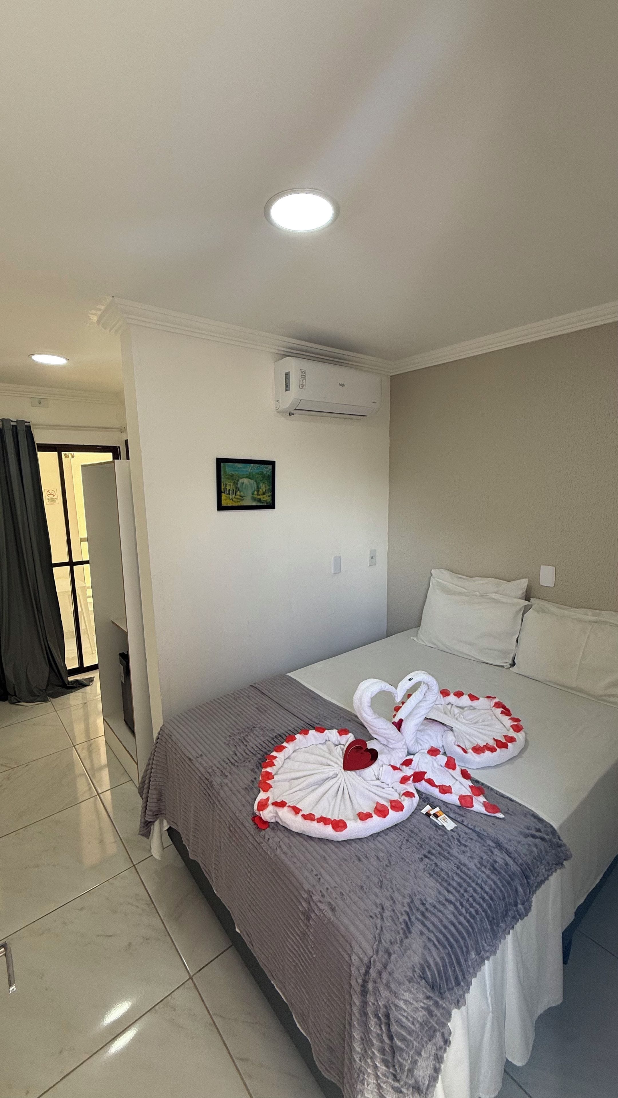 A hotel room with a bed, a picture on the wall, and an air conditioning unit.