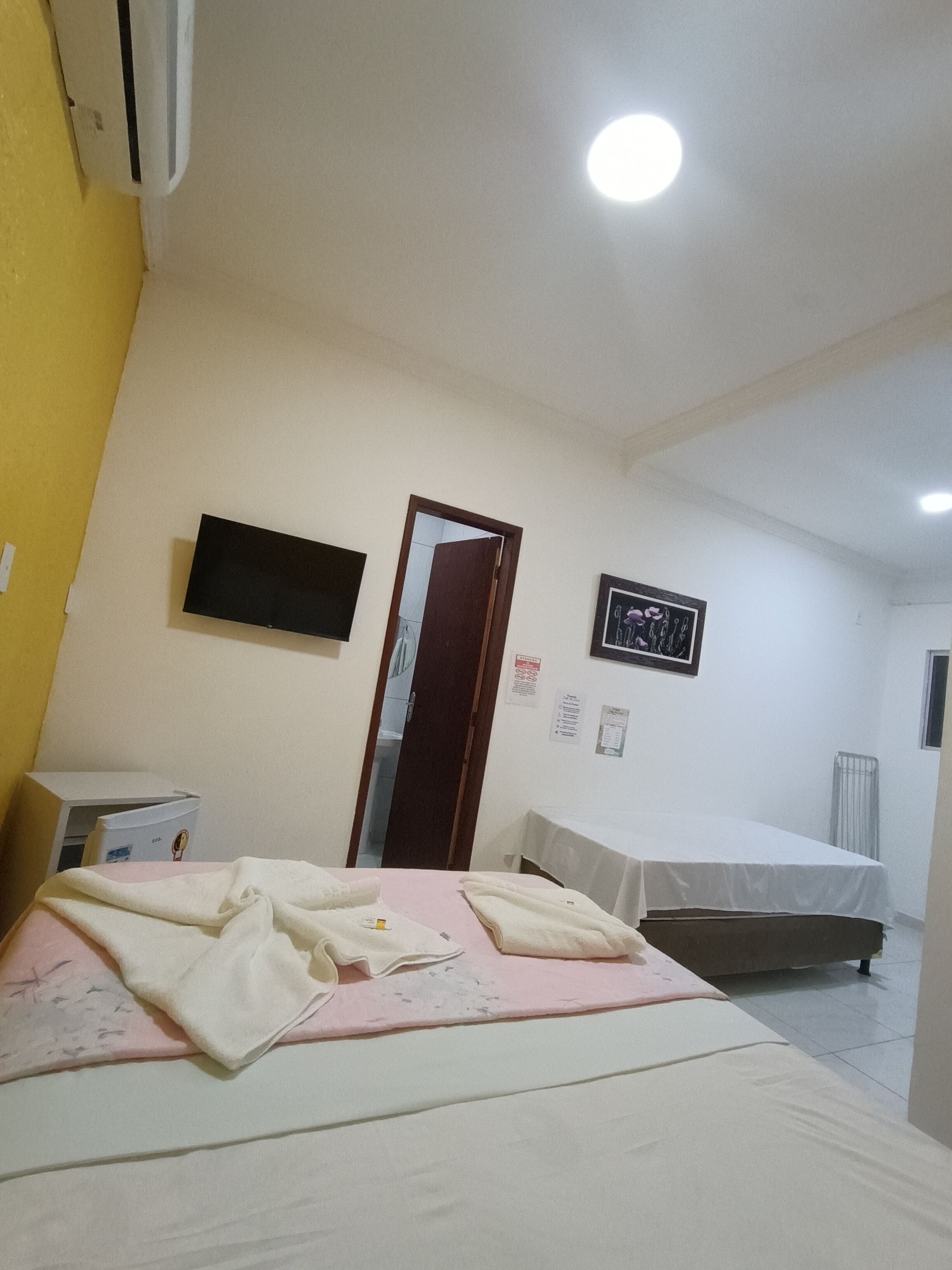 Quarto de hotel com cama, mesa de cabeceira e televisão na parede.