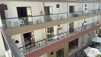 Un hotel de varios niveles con barandillas de cristal, mobiliario exterior y tejado de tejas rojas.