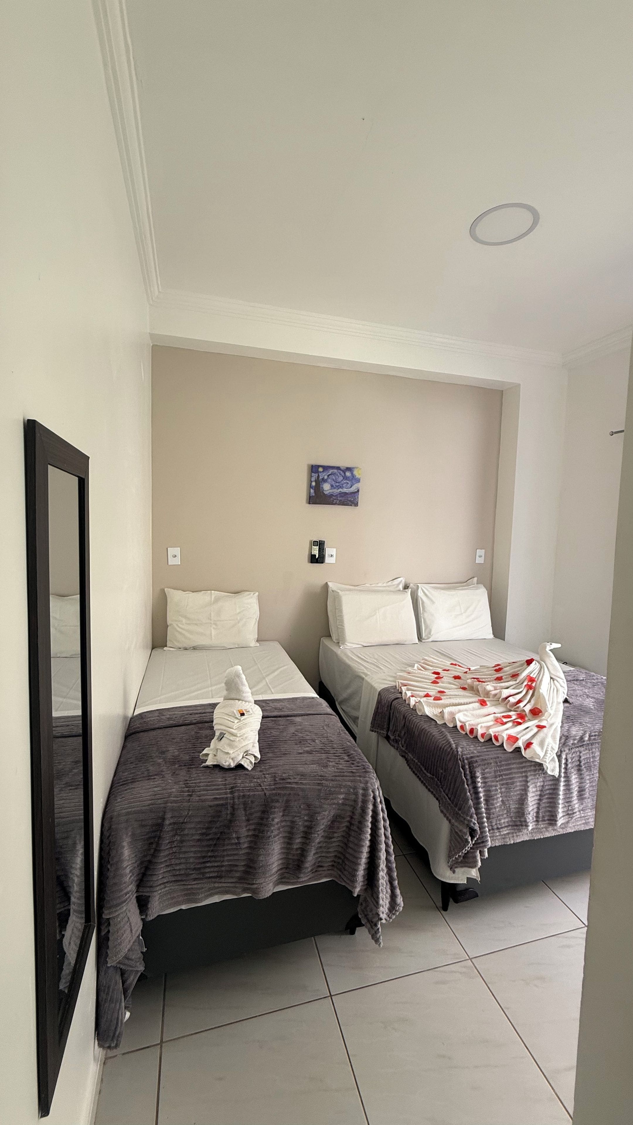 A room with two beds, a mirror, a painting, and a telephone on the wall.