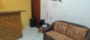 A room with a brick fireplace, a wicker sofa, a small table with a basket, and a black suitcase.
