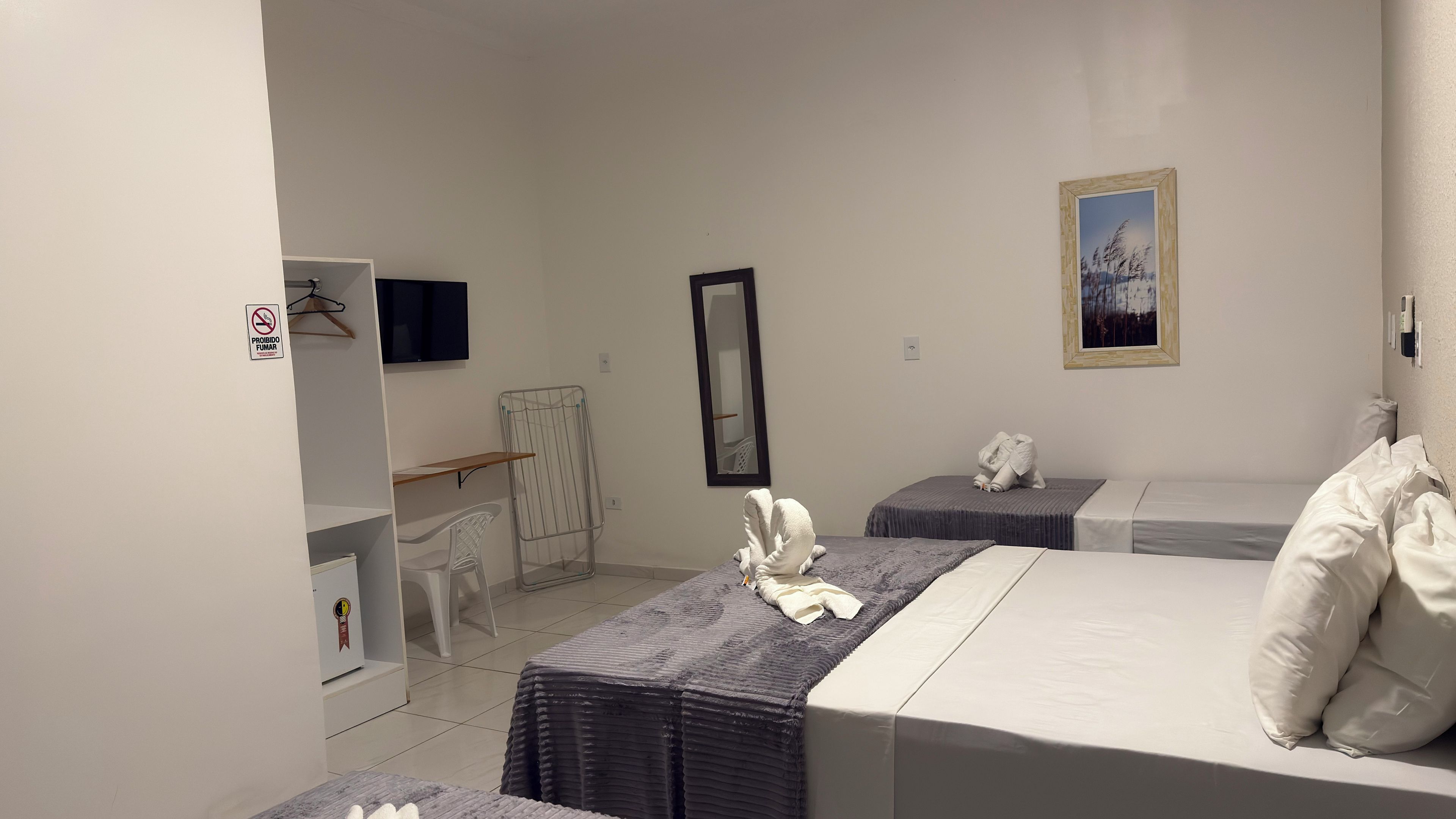 A hotel room with two beds, a TV, a mirror, a painting, and a towel rack.