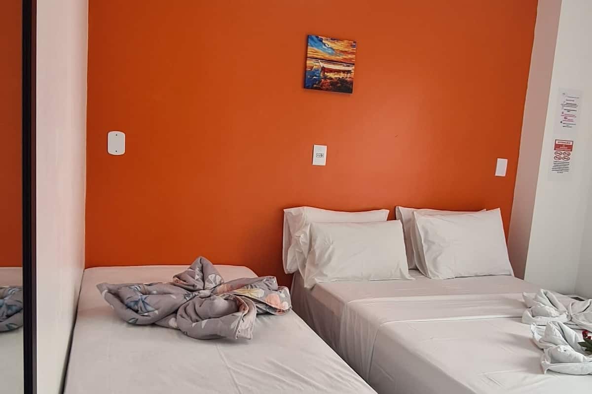 Ein Hotelzimmer mit zwei Betten, einer orangefarbenen Akzentwand und einem kleinen Gemälde.