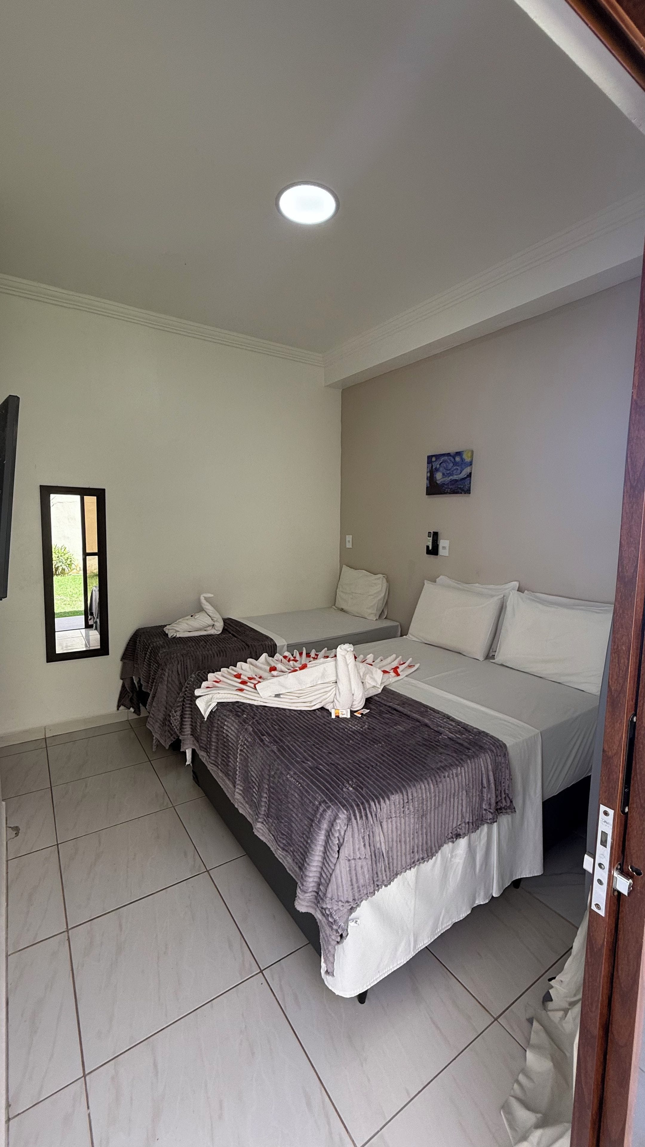 A hotel room with two beds, a mirror, a painting, and a ceiling light.