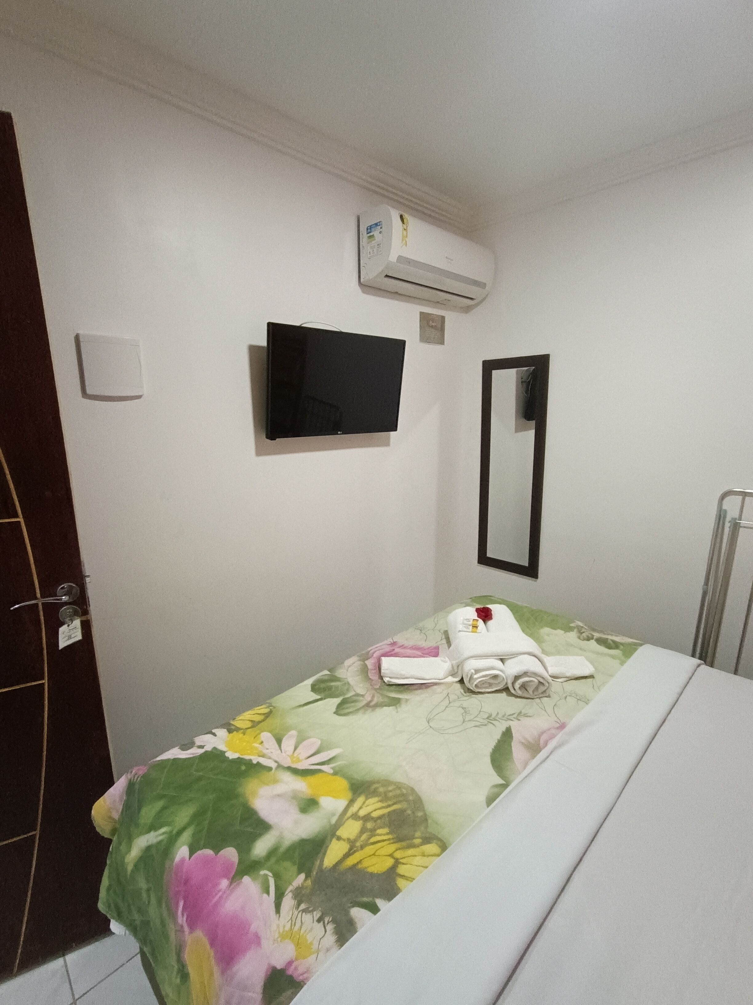 A hotel room with a bed, a TV, an air conditioner, a mirror, and a door.