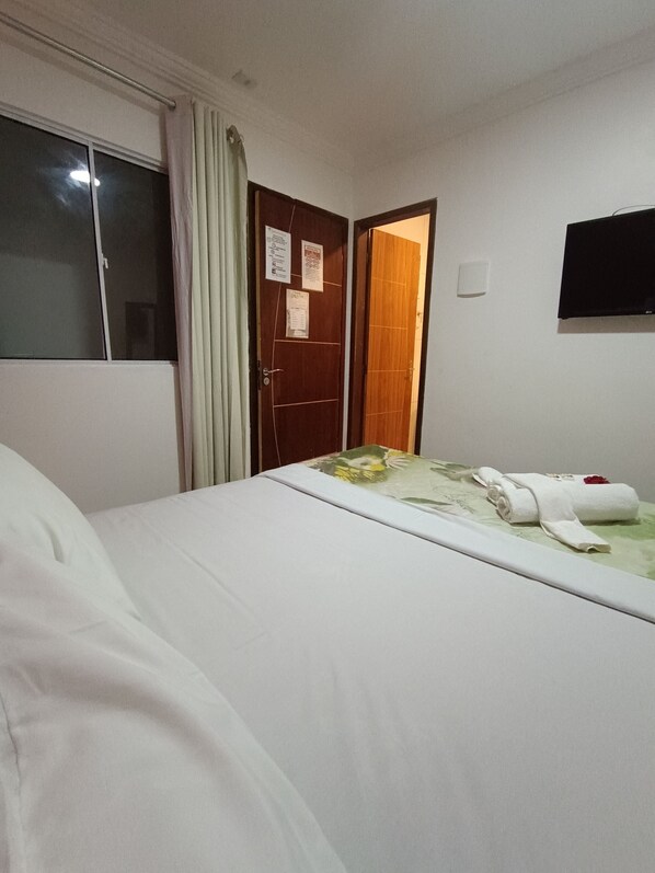A hotel room with a bed, a door with a notice, a flat-screen TV on the wall, and a window with curtains. - Pousada Canto dos Corais Maragogi (Maragogi)