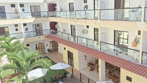 Een meerlaags gebouw met balkons, buitenmeubels en een binnentuin met palmbomen.