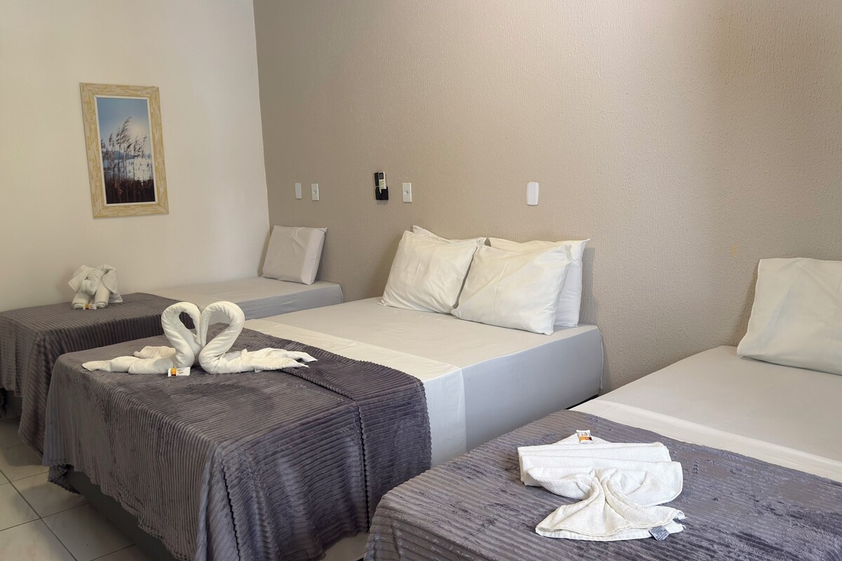 A hotel room with two single beds, each with a gray bedspread and white pillows. There is a framed picture on the wall above the left bed.