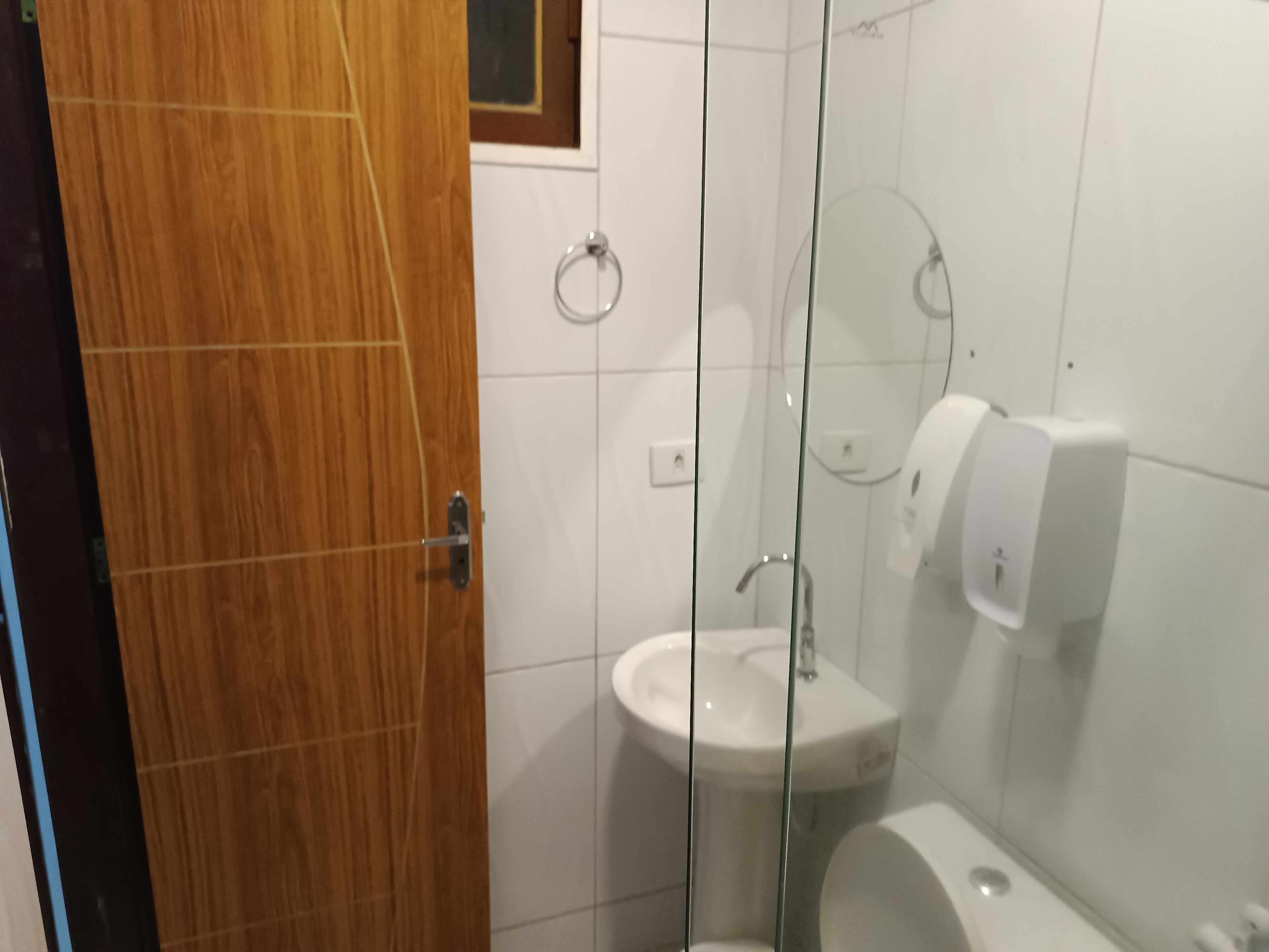 A bathroom with a wooden door, a white sink, a glass shower enclosure, and a hand dryer.