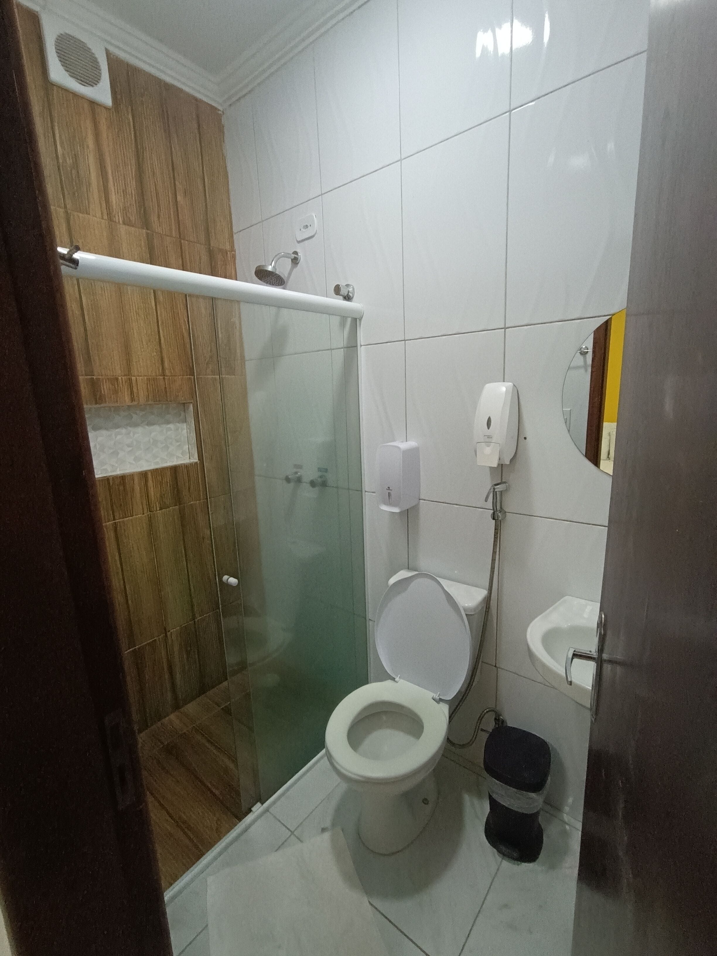 A bathroom with a glass-enclosed shower, a toilet, a sink, and a soap dispenser.