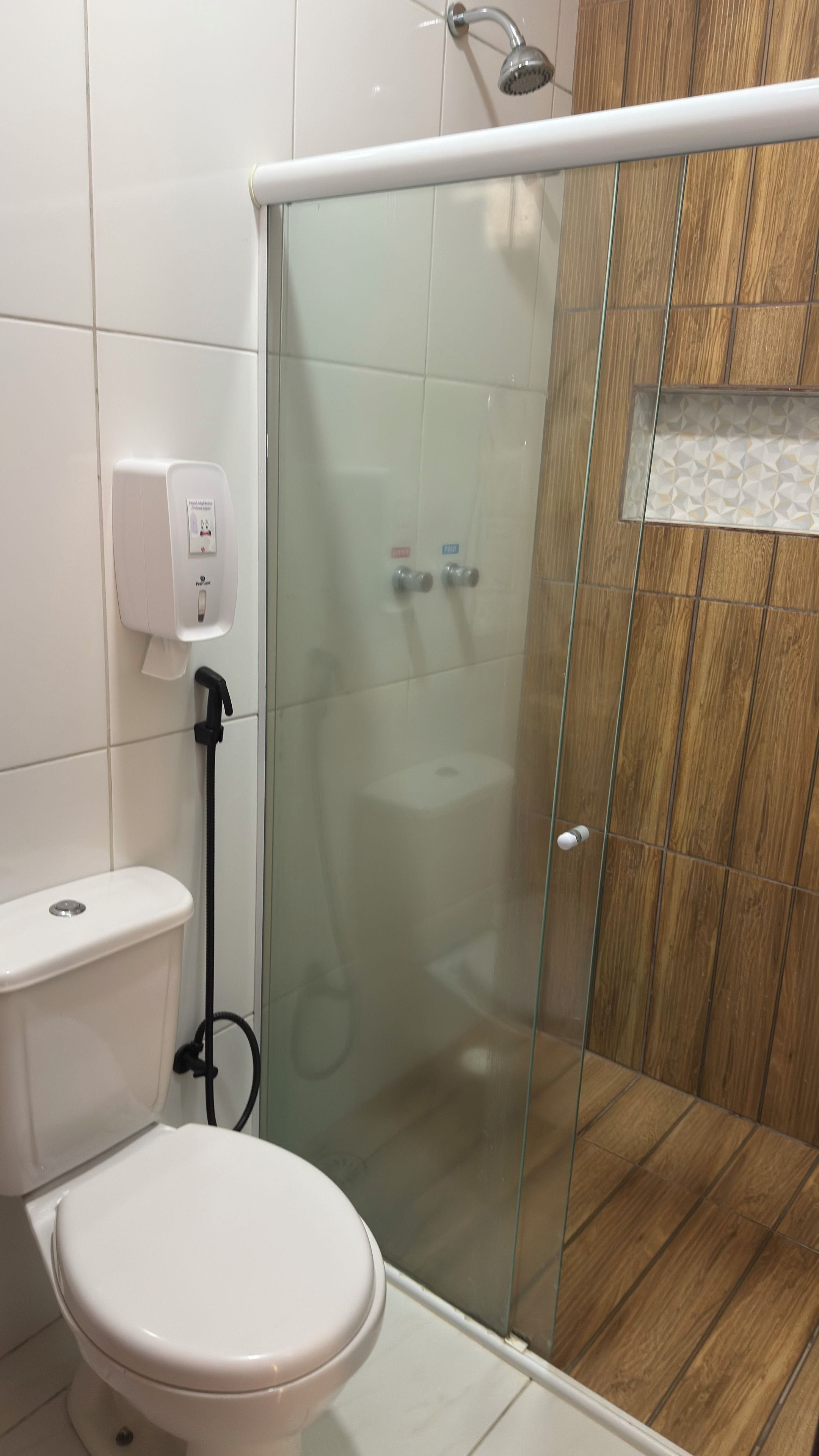 A bathroom with a toilet, a glass shower enclosure, and a hand dryer.