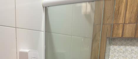 A bathroom with a toilet, a glass shower enclosure, and a hand dryer.