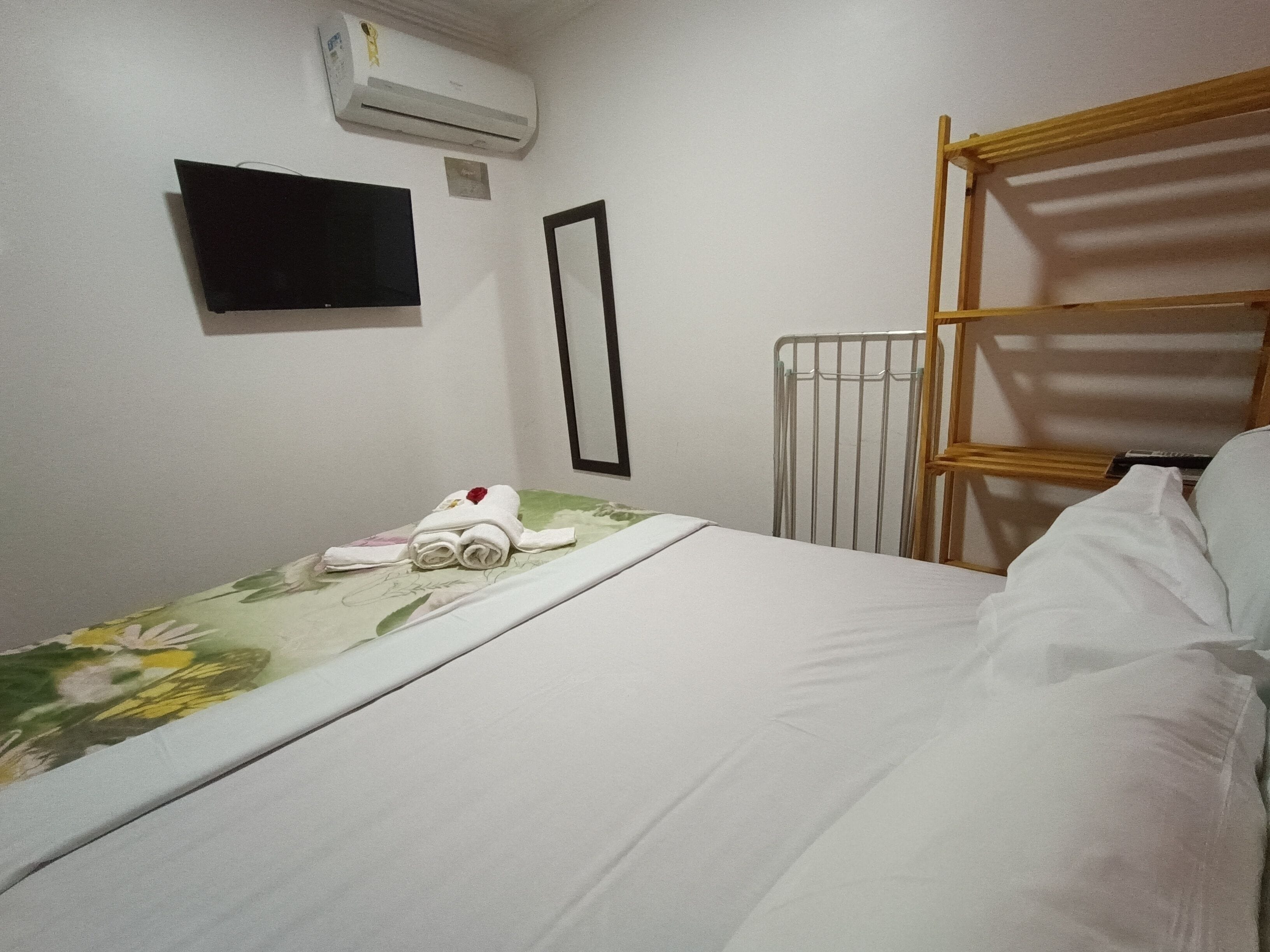 A hotel room with a bed, a TV mounted on the wall, an air conditioner, and a radiator.