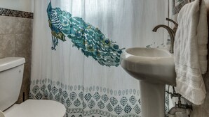 Un baño con cortina de ducha con motivos de pavo real, un lavamanos pedestal y un inodoro.