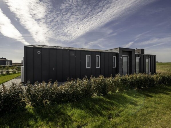 A modern, black, modular building with a flat roof, large windows, and a small entrance.