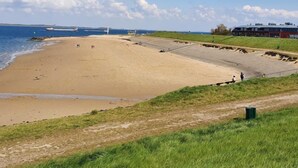 Ein Strand mit befestigtem Gehweg, einer Grünfläche und einem Gebäude im Hintergrund.