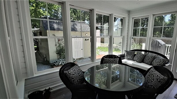 Une véranda avec une table et des chaises en verre, de grandes fenêtres et une vue sur le jardin arrière.