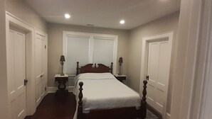 Une petite chambre avec un lit simple, une tête de lit en bois, deux tables de chevet avec des lampes et une fenêtre avec des stores.