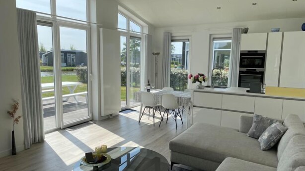 Ein modernes Wohnzimmer mit einem Glastisch, einem grauen Sofa und einem Essbereich mit weißem Tisch und Stühlen.