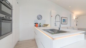 Eine moderne Küche mit weißen Schränken, einem eingebauten Backofen, einem Spülbecken mit Armatur und einer Uhr an der Wand.