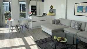 Ein modernes Wohnzimmer mit grauem Sofa, einem Glastisch und einem Essbereich mit Tisch und Stühlen.