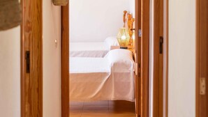 Ein Flur, der in ein Schlafzimmer mit Bett, Lampe und hängender Pflanze führt.