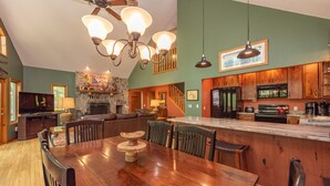 A spacious kitchen with a large island, wooden cabinets, and a stone fireplace. - Cozy Cove Retreat w/ Arcade & Fireplace (Oakland)