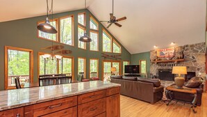 A spacious living area with a large wooden dining table, a fireplace, and a stone accent wall. - Cozy Cove Retreat w/ Arcade & Fireplace (Oakland)
