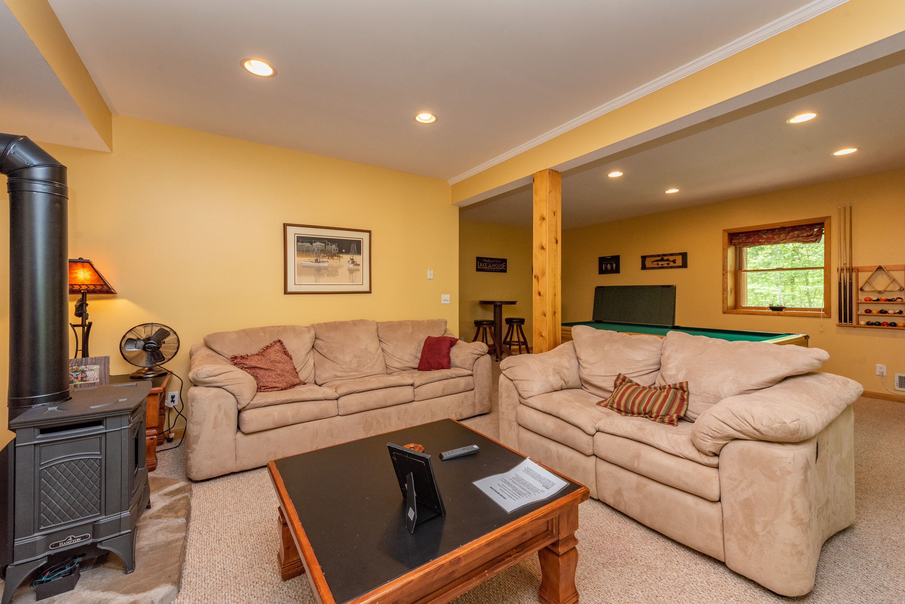 A living room with two beige sofas, a black table, a wood-burning stove, and a pool table in the background.