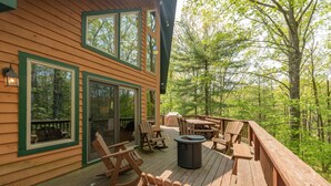 A wooden deck with outdoor furniture, including chairs and a table, overlooking a forested area. - Cozy Cove Retreat w/ Arcade & Fireplace (Oakland)