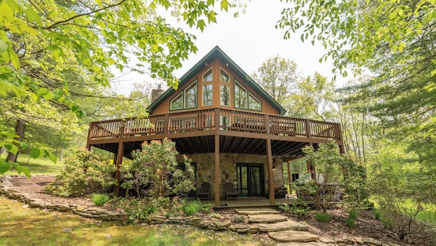 A cabin with a stone foundation, wooden deck, and a covered porch. - Cozy Cove Retreat w/ Arcade & Fireplace (Oakland)