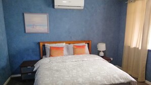 A bedroom with a bed, a nightstand, an air conditioner, a lamp, and a window with curtains. - Cosy and immaculate 3-bedroom home (Lynwood)