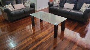 A living room with two dark leather sofas, a glass coffee table, and wooden flooring. - Cosy and immaculate 3-bedroom home (Lynwood)