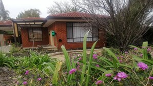 A residential building with a brick facade, a covered porch, and a garden with purple flowers. - Cosy and immaculate 3-bedroom home (Lynwood)