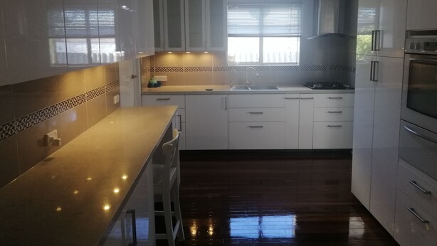 A modern kitchen with white cabinets, a stainless steel countertop, a built-in oven, and a window with blinds. - Cosy and immaculate 3-bedroom home (Lynwood)