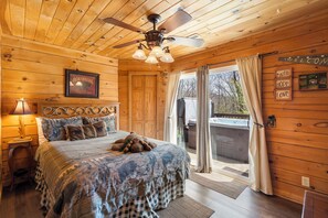 A wooden cabin bedroom with a bed, a ceiling fan, a framed picture, and a sliding glass door leading to an outdoor area. - Traditional Log Cabin Near Big Cedar, PVT Fire Pit, Hot Tub, Scenic Woods, Trails End, Free Tickets! (Ridgedale)
