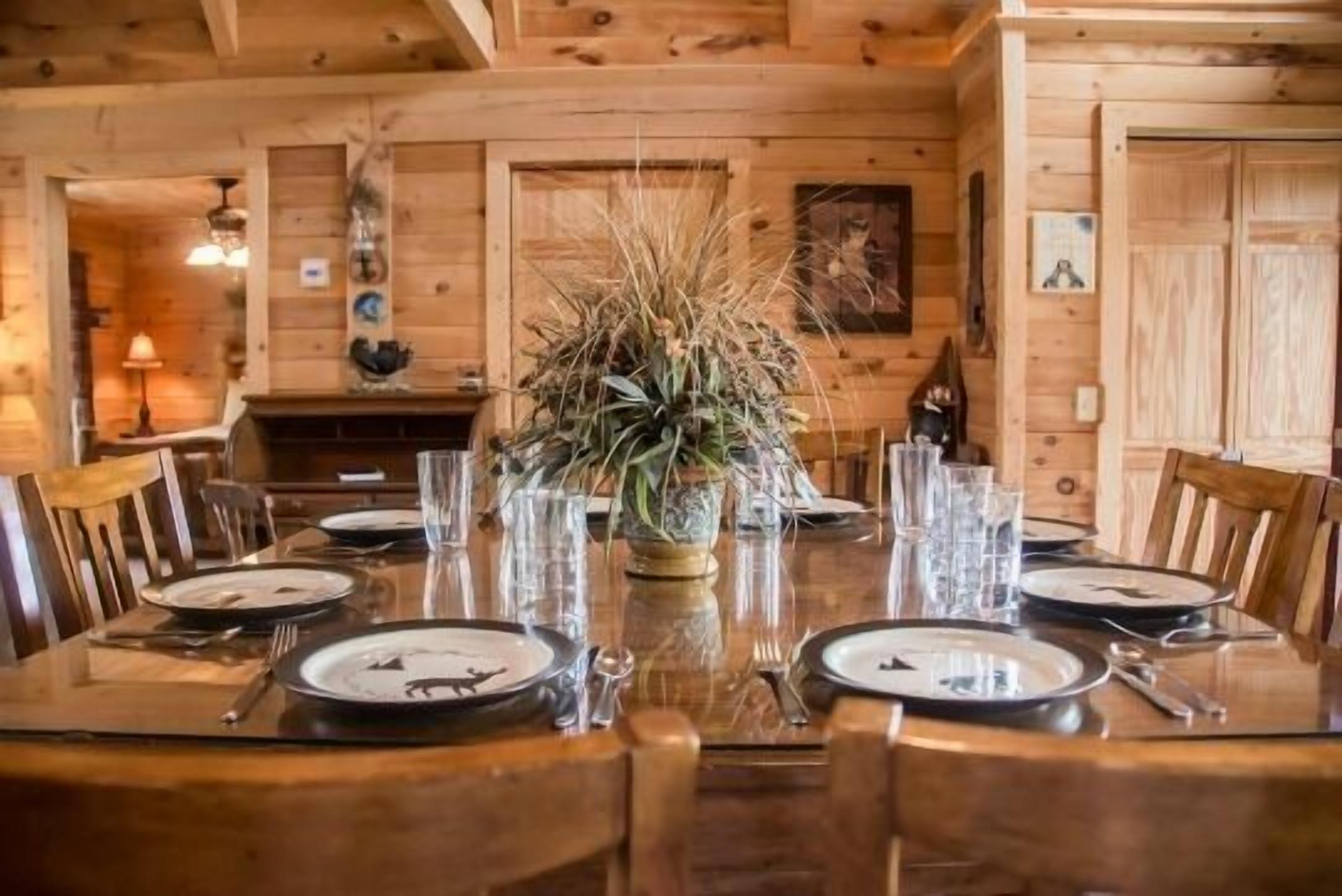A wooden dining table set for four with a centerpiece of dried plants.