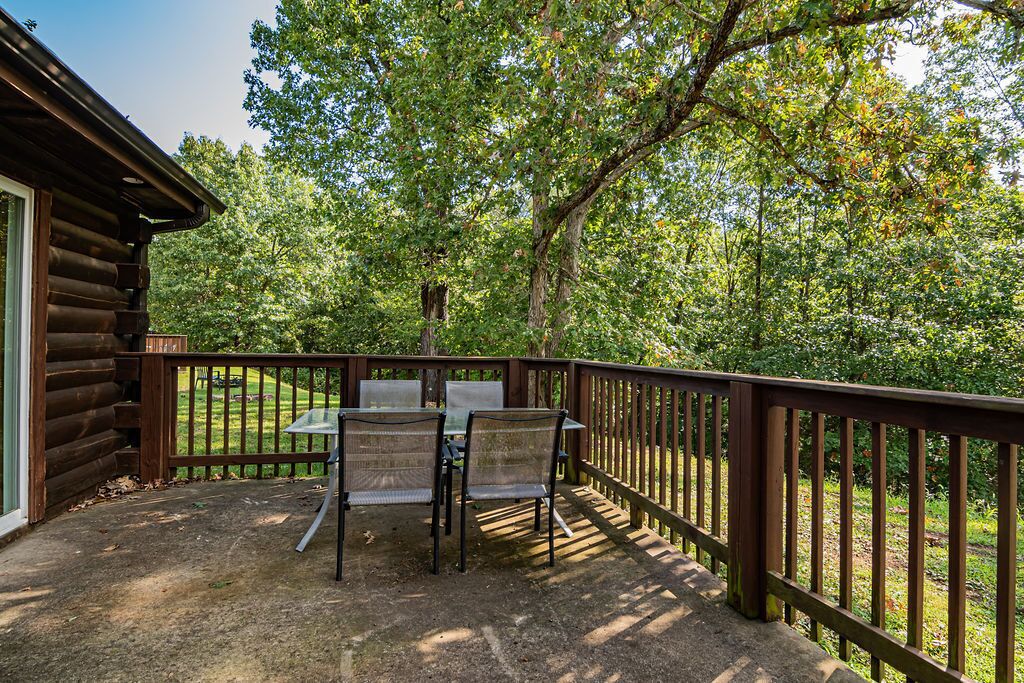 A wooden deck with a table and chairs, surrounded by a wooden railing, overlooking a forested area.