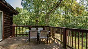 A wooden deck with a table and chairs, surrounded by a wooden railing, overlooking a forested area.