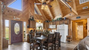 A wooden cabin interior with a dining area, kitchen, and a large window. - Traditional Log Cabin Near Big Cedar, PVT Fire Pit, Hot Tub, Scenic Woods, Trails End, Free Tickets! (Ridgedale)