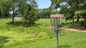 A disc golf basket with a sign, surrounded by a grassy field and trees.