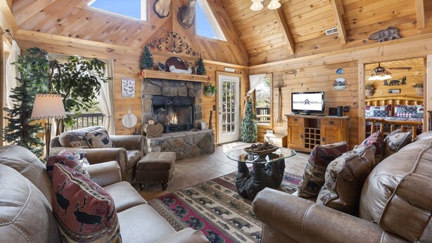 A log cabin interior with a stone fireplace, leather furniture, and deer antlers on the ceiling. - Traditional Log Cabin Near Big Cedar, PVT Fire Pit, Hot Tub, Scenic Woods, Trails End, Free Tickets! (Ridgedale)