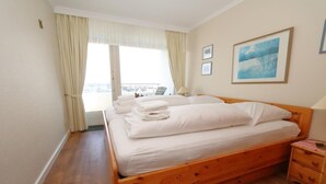 A hotel room with a wooden bed, a view of the city through large windows, and a framed picture on the wall.