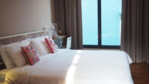 A hotel room with a large bed, a bedside table with a lamp, a fan, and a view of the sky through the window.