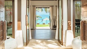 A hallway leading to a beach view with a thatched umbrella, a large vase, and a wooden door frame. - HSH - 3 Bedrooms Front Beach - Bangrak (Koh Samui)