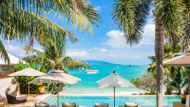 A poolside view with lounge chairs, umbrellas, and a clear view of the ocean and distant island. - HSH - 3 Bedrooms Front Beach - Bangrak (Koh Samui)